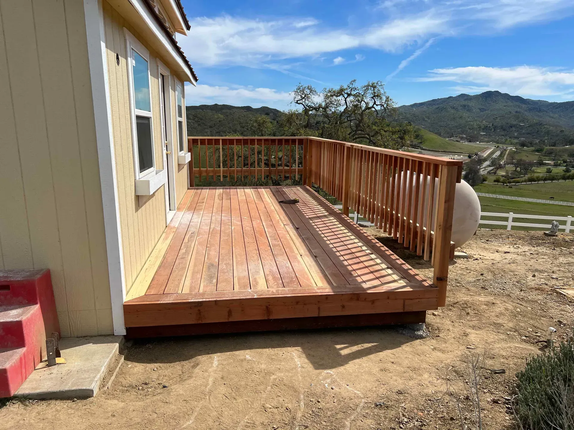 A wooden deck is sitting on top of a dirt hill next to a house.
