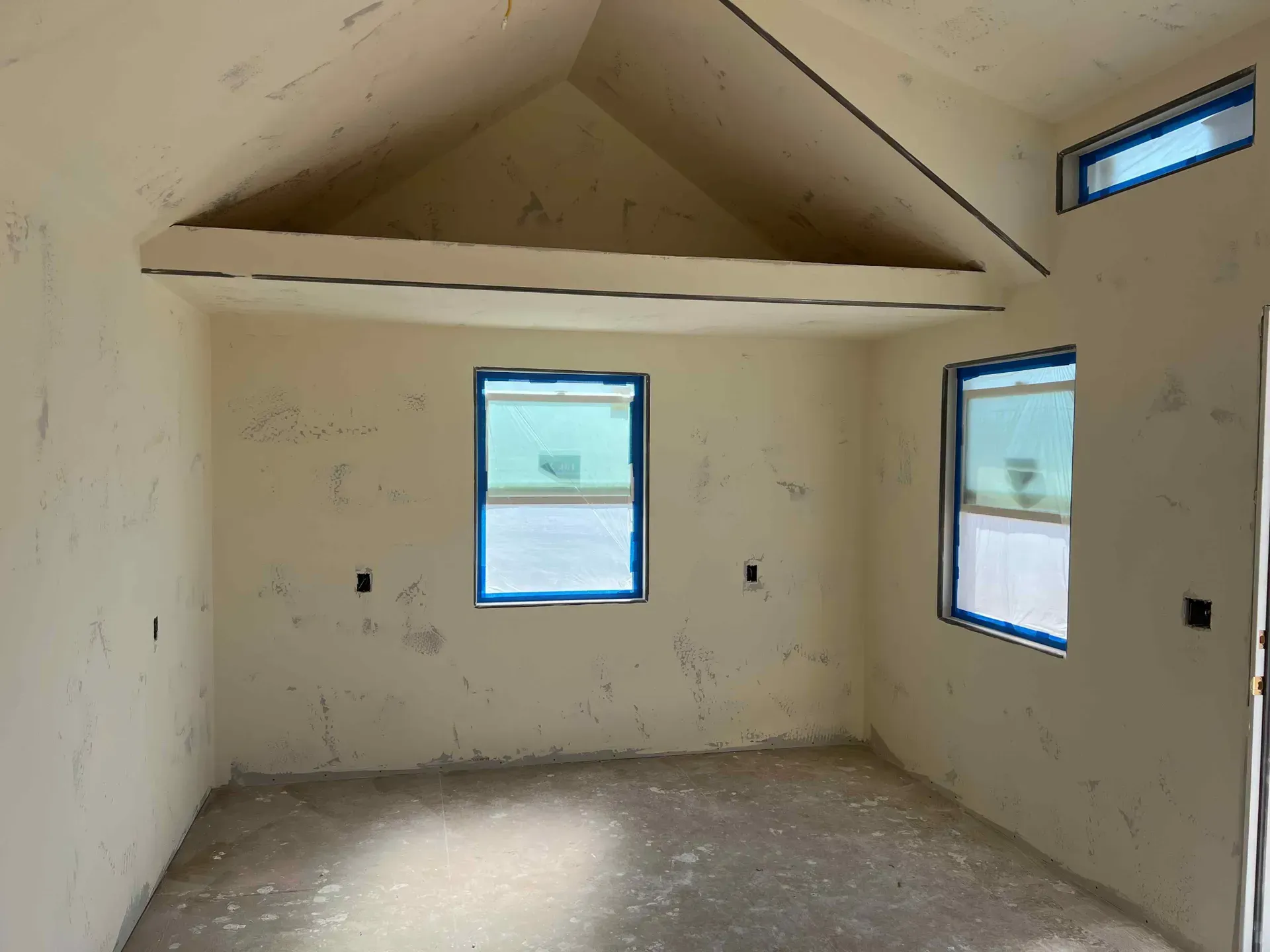 An empty room with a vaulted ceiling and two windows.