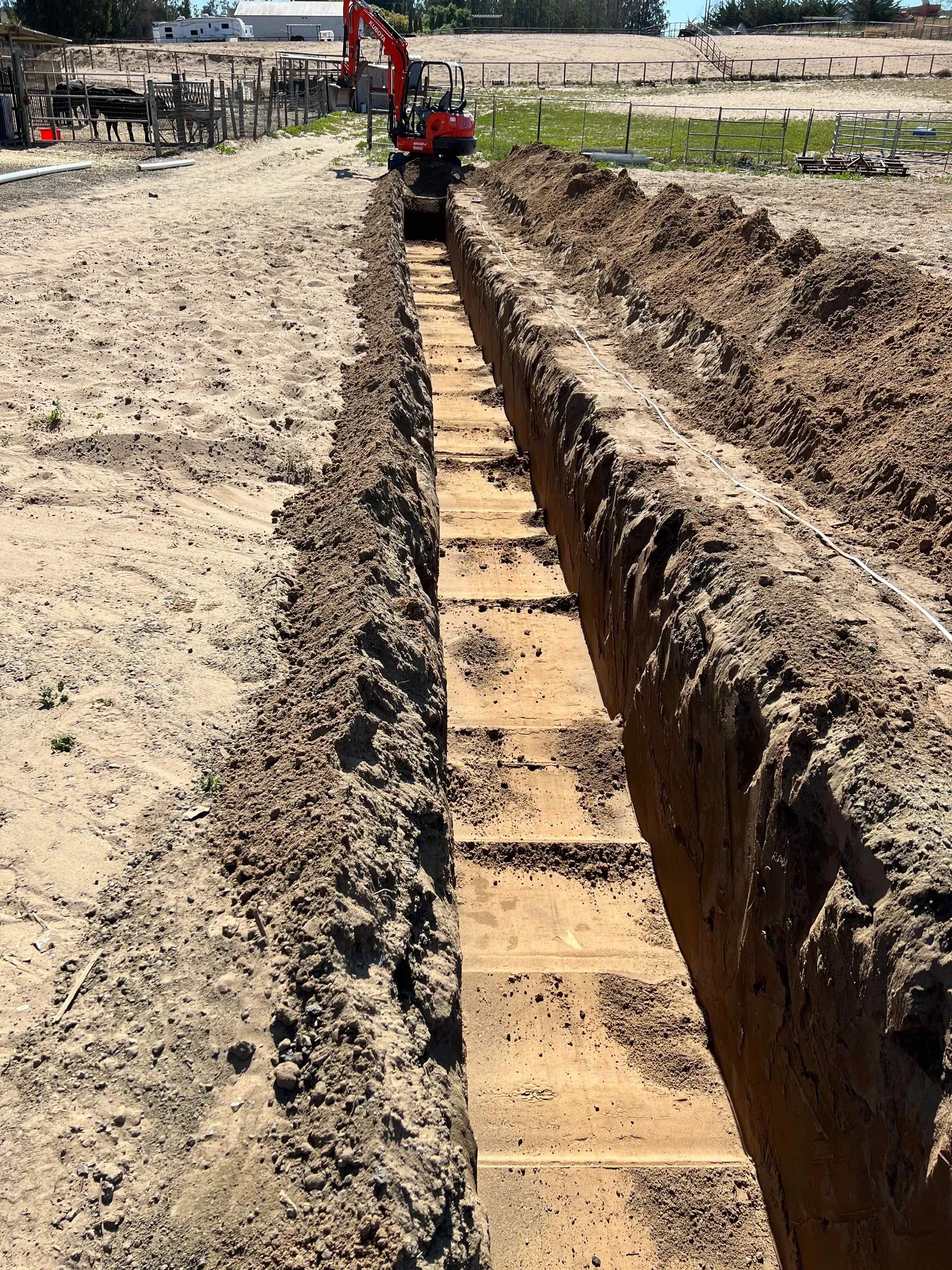 A red excavator is digging a trench in the dirt.