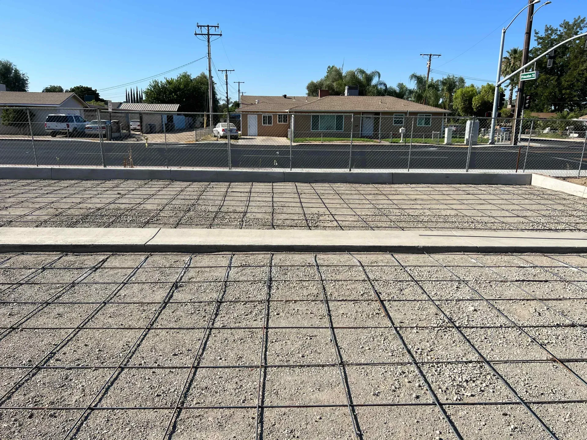 A concrete driveway with a fence and houses in the background