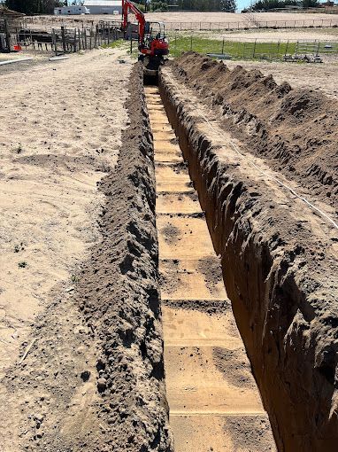 A red excavator is digging a trench in the dirt.