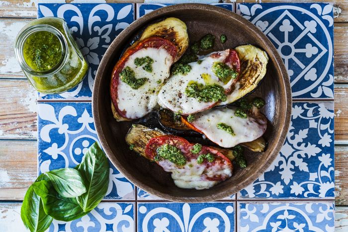 A bowl of vegetables with cheese and pesto on a table.