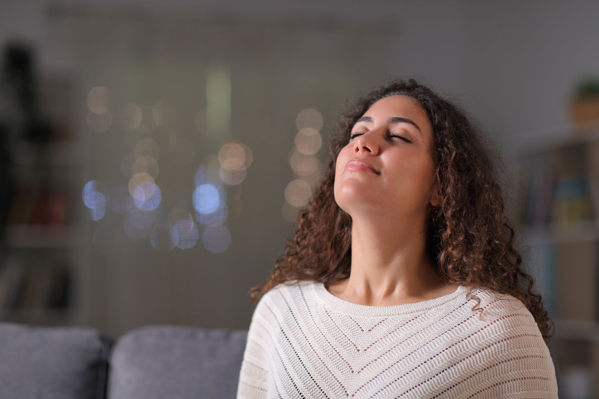 A woman is sitting on a couch with her eyes closed.