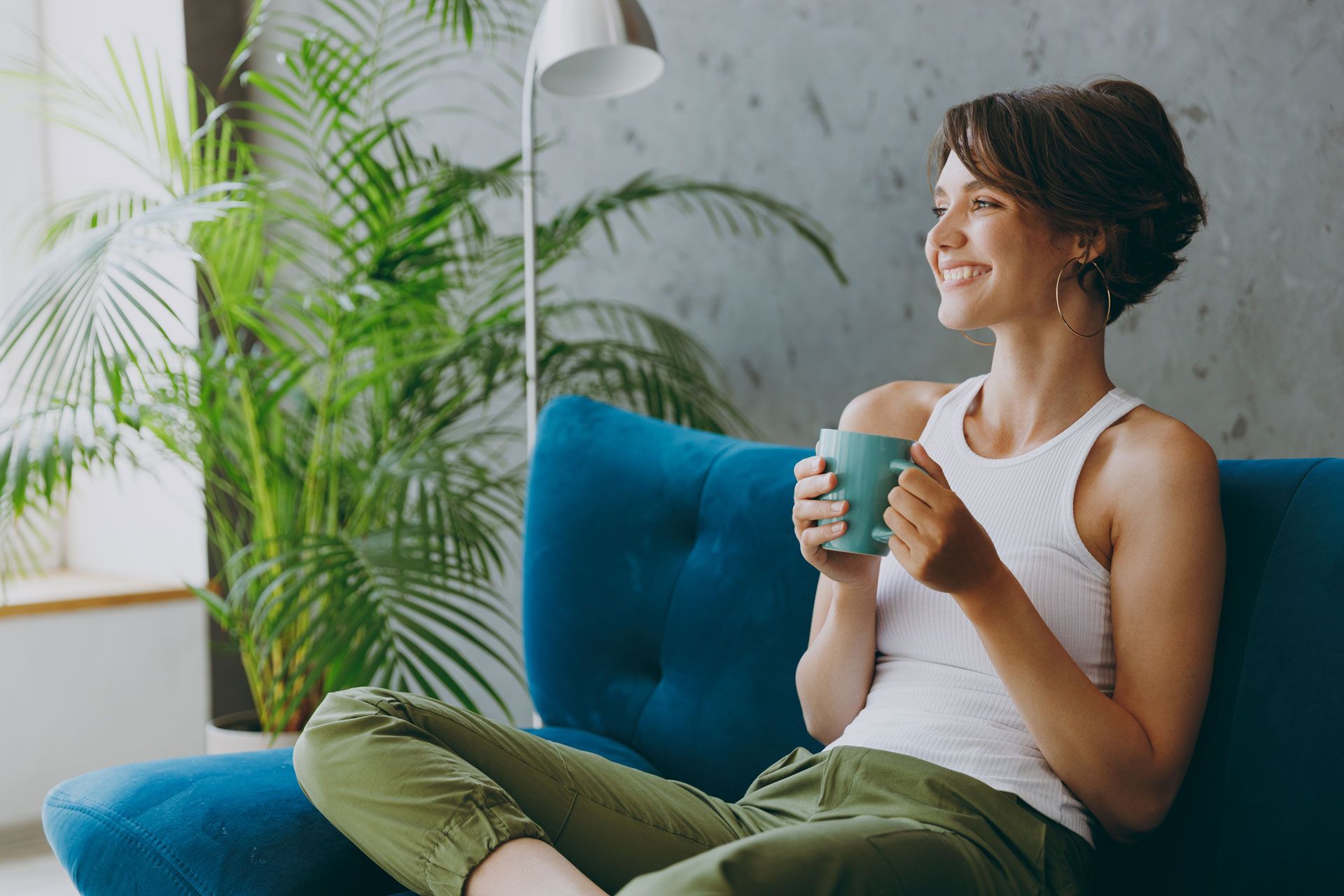 A woman is sitting on a blue couch holding a cup of coffee.