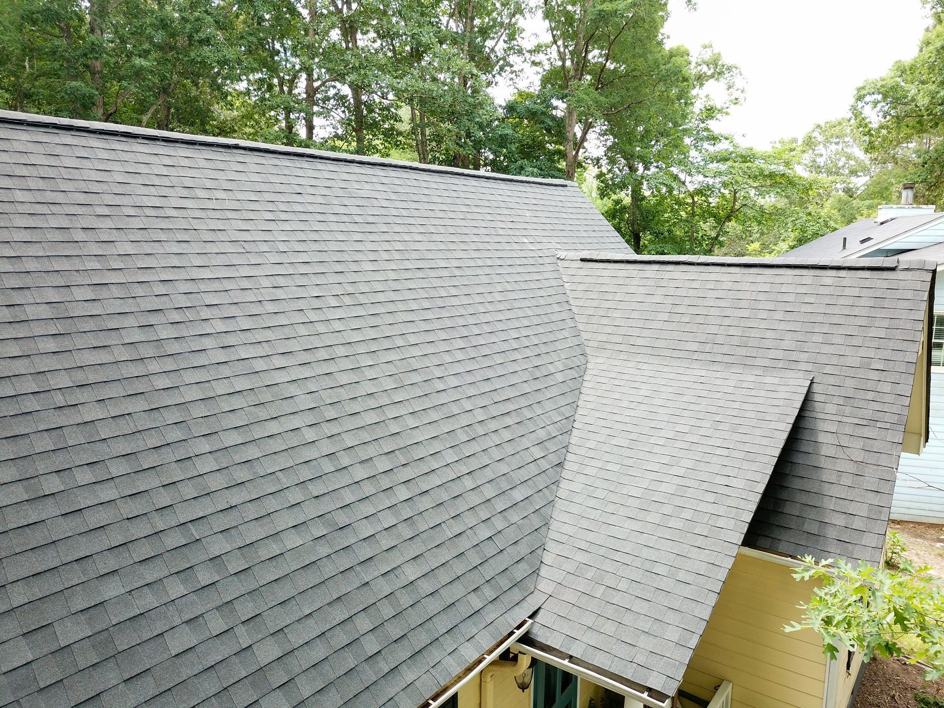 Grey shingle roof with multiple angles against a backdrop of green trees.