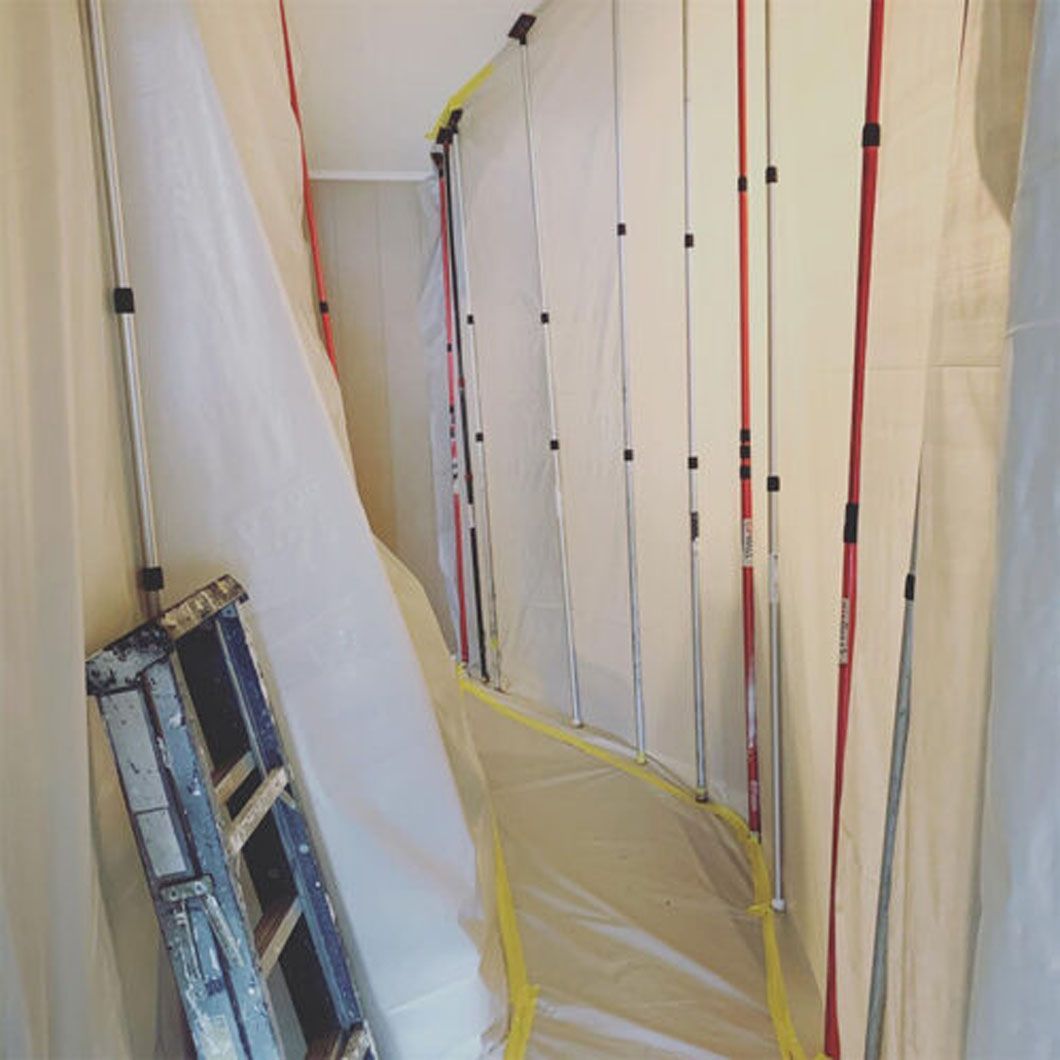 A ladder is leaning against a wall in a hallway covered in tarps.