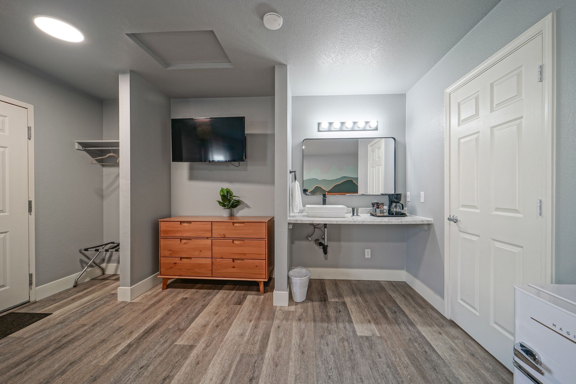 Bright bathroom vanity with mirror, white walls, wood dresser cabinet, wall-mounted TV, and closet doors