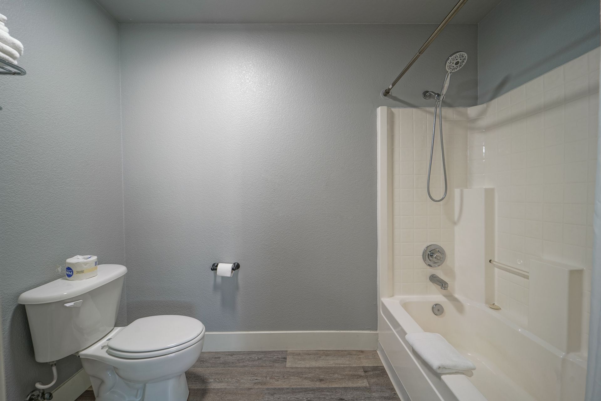Small bathroom with toilet, sink, and white tub-shower against gray walls.