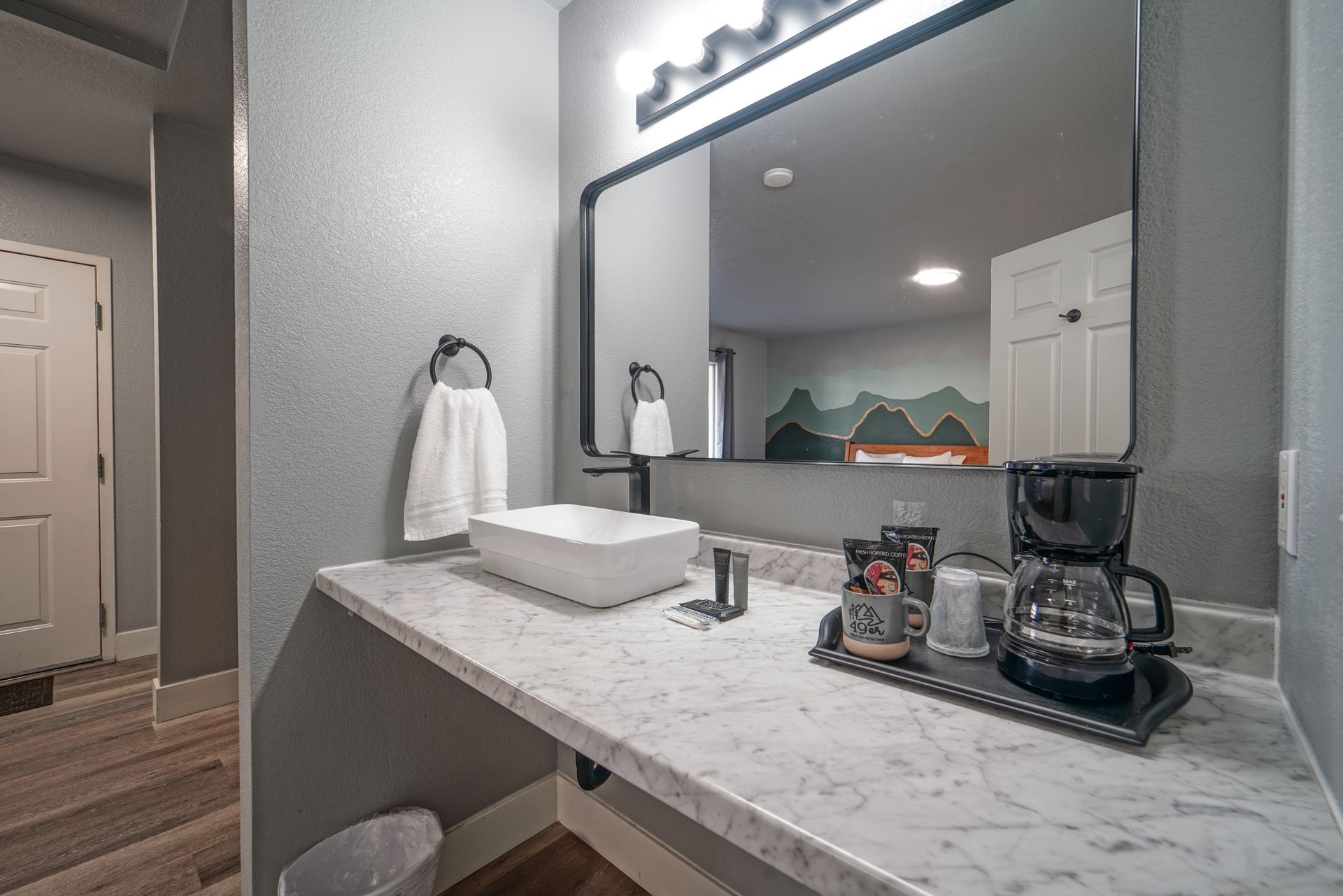 Bathroom vanity with marble countertop, mirror, towels, and coffee maker on a tray.