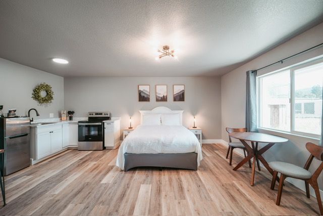 Studio apartment with bed, small kitchen, dining table, and large window.