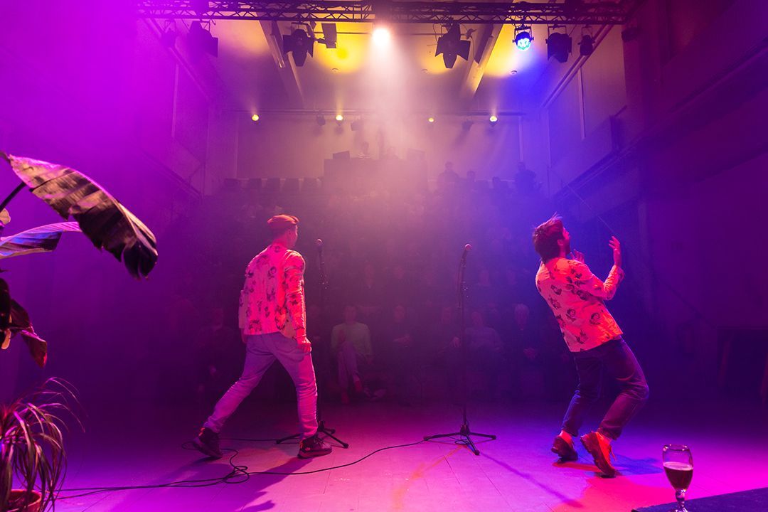 Twee mannen dansen op een podium met paarse lichten