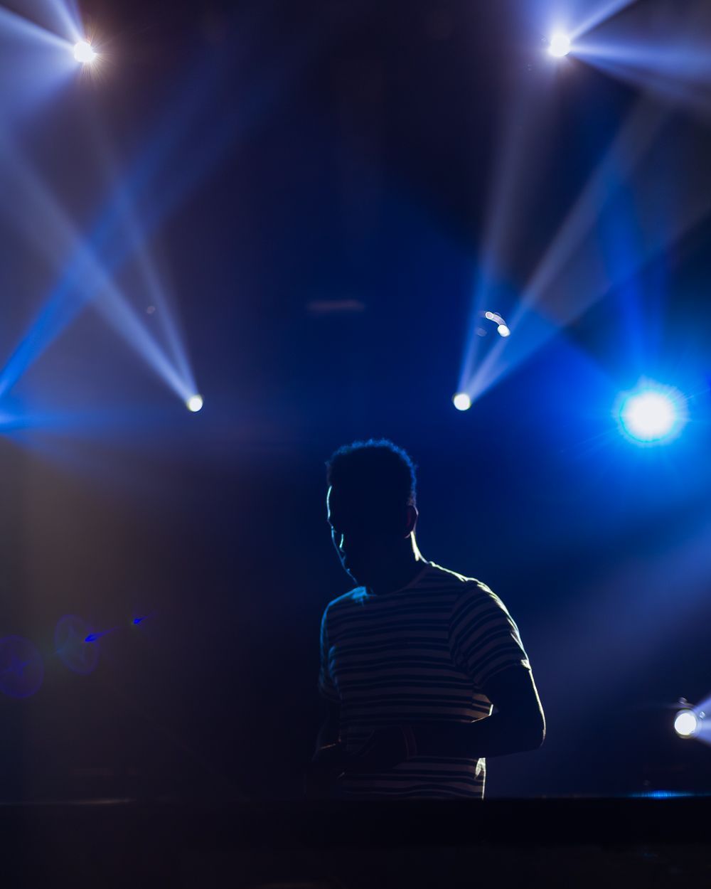 Silhouet van een persoon voor felblauwe podiumlichten. Draagt ​​een gestreept shirt.