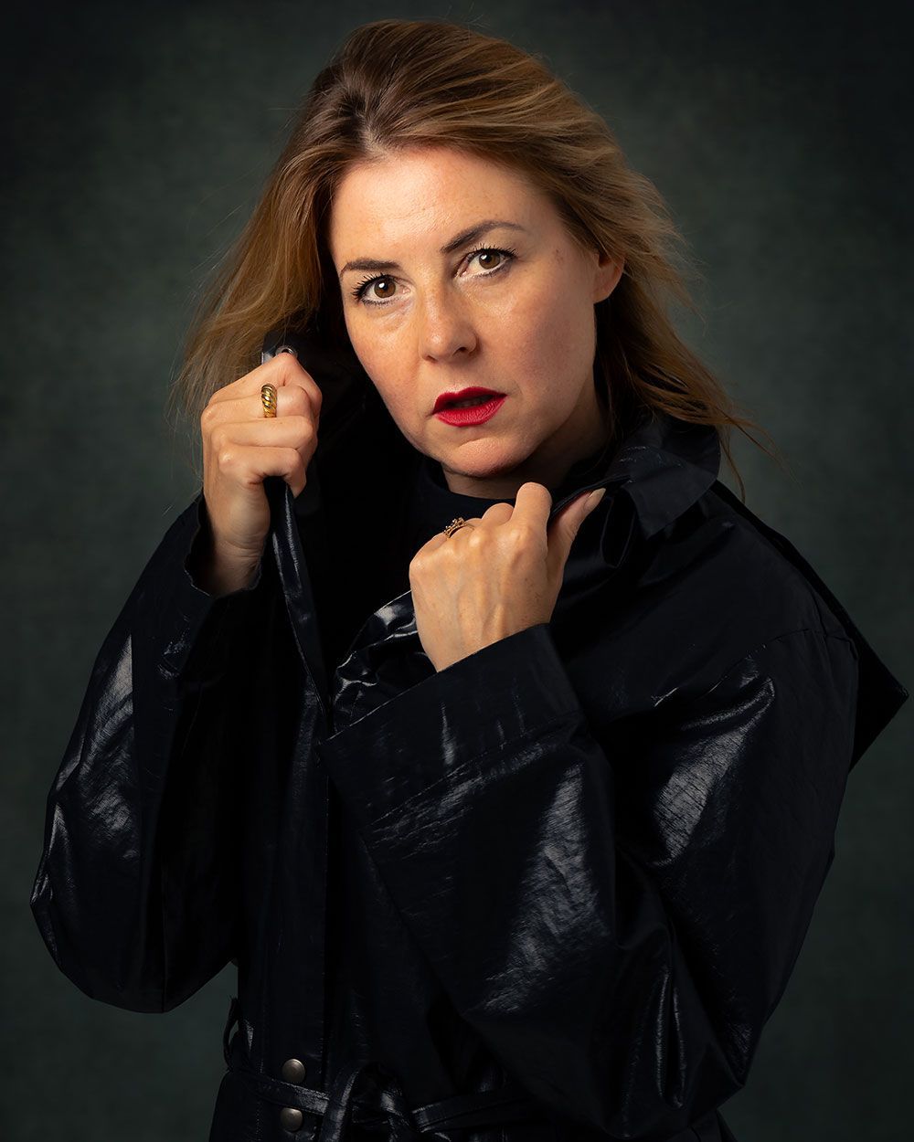 Vrouw in een zwarte jas, met een opstaande kraag, rode lippenstift, kijkt recht in de camera.
