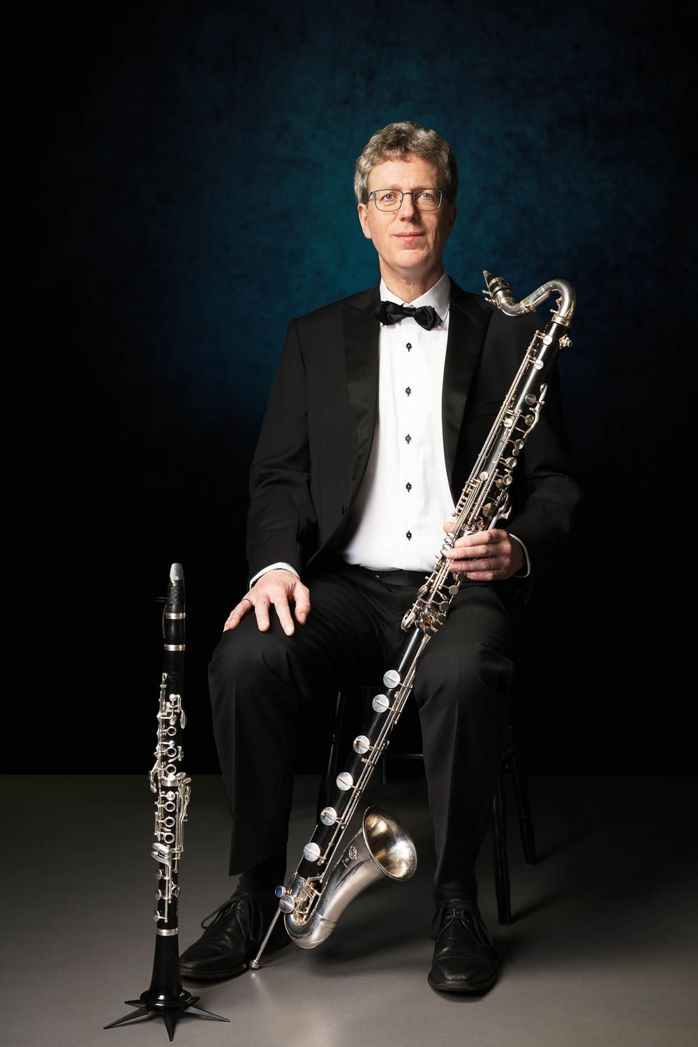 Een vrouw met krullend donker haar glimlacht, gekleed in een olijfgroen vest en een top met patroon.