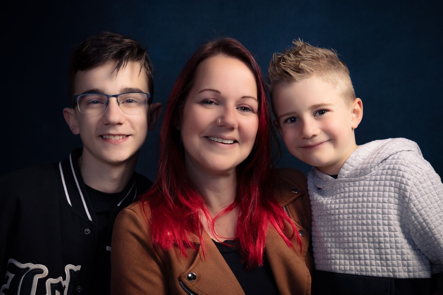 Lachende vrouw met rood haar en twee kinderen tegen een donkerblauwe achtergrond.