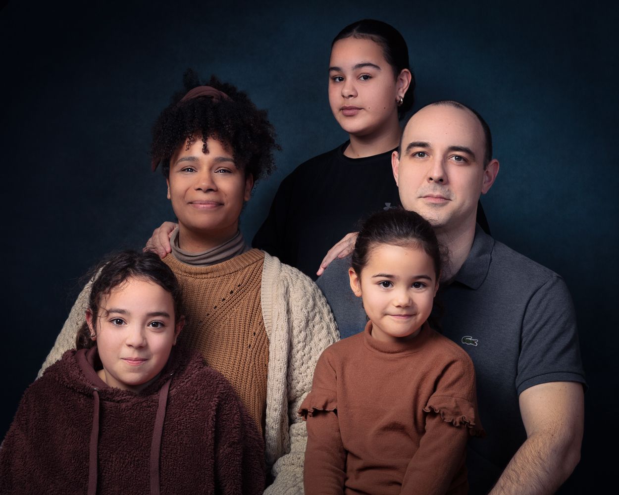 Een gezin van vijf lacht naar de camera tegen een donkerblauwe achtergrond.