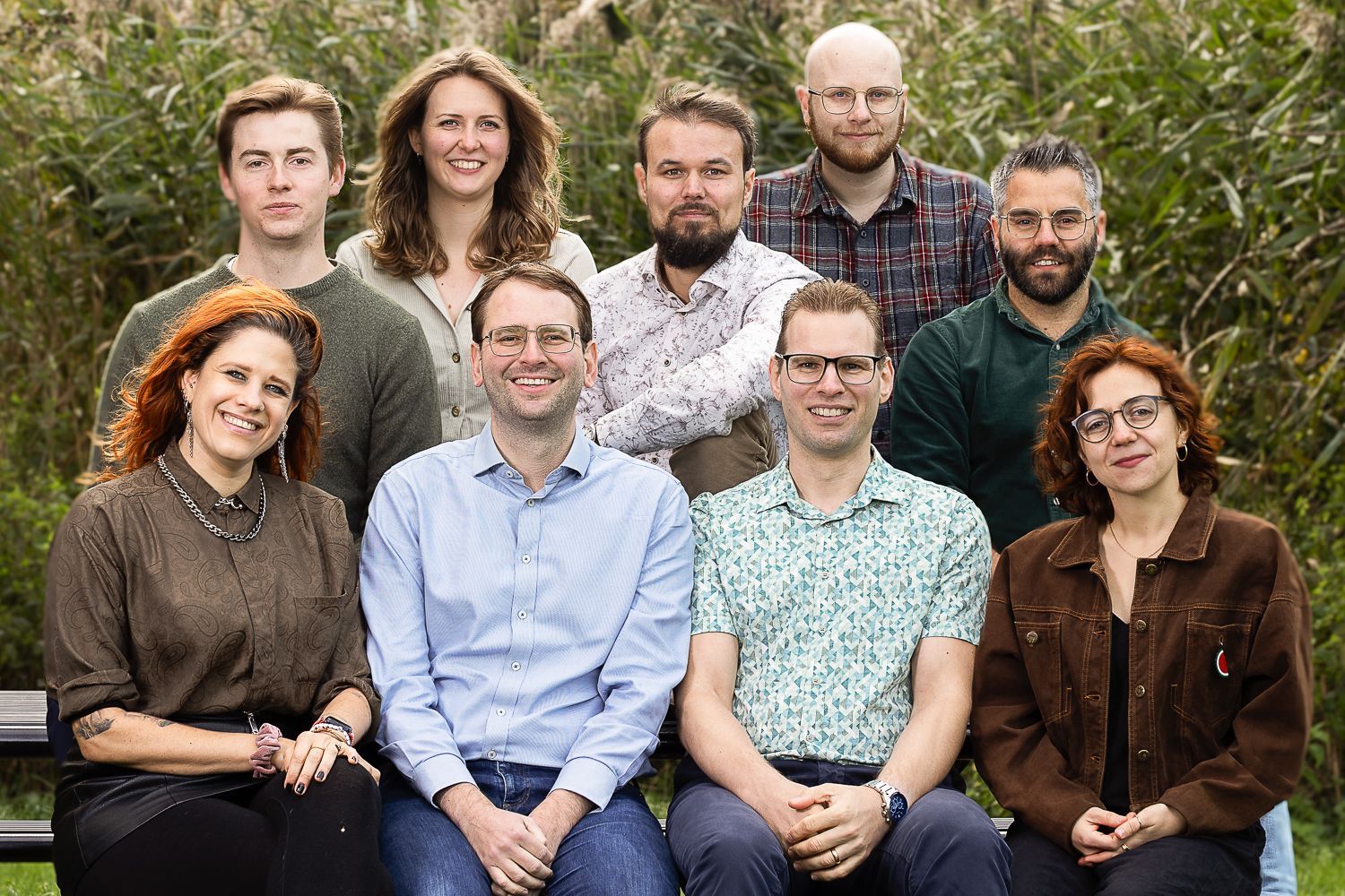 Een groep van negen mensen poseert voor een foto buiten bij het hoge gras.