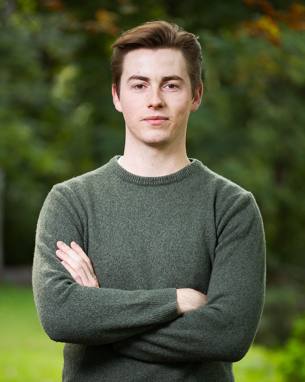 Man met gekruiste armen in een groene trui tegen een wazige groene achtergrond.