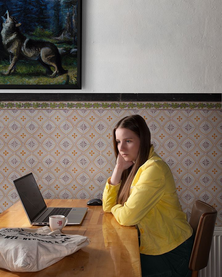 Een vrouw in een geel jasje zit aan een tafel met een laptop