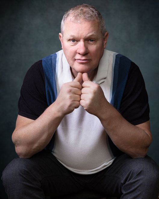 Een man in een zwart shirt en een blauw vest hurkt neer