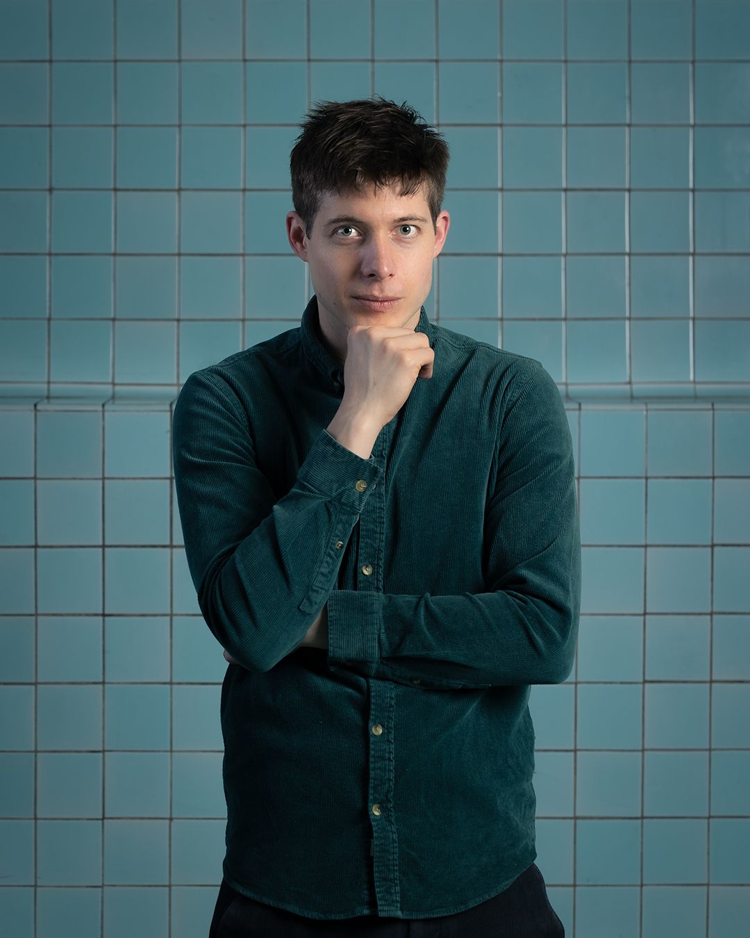 Een man in een groen shirt staat voor een blauwe betegelde muur