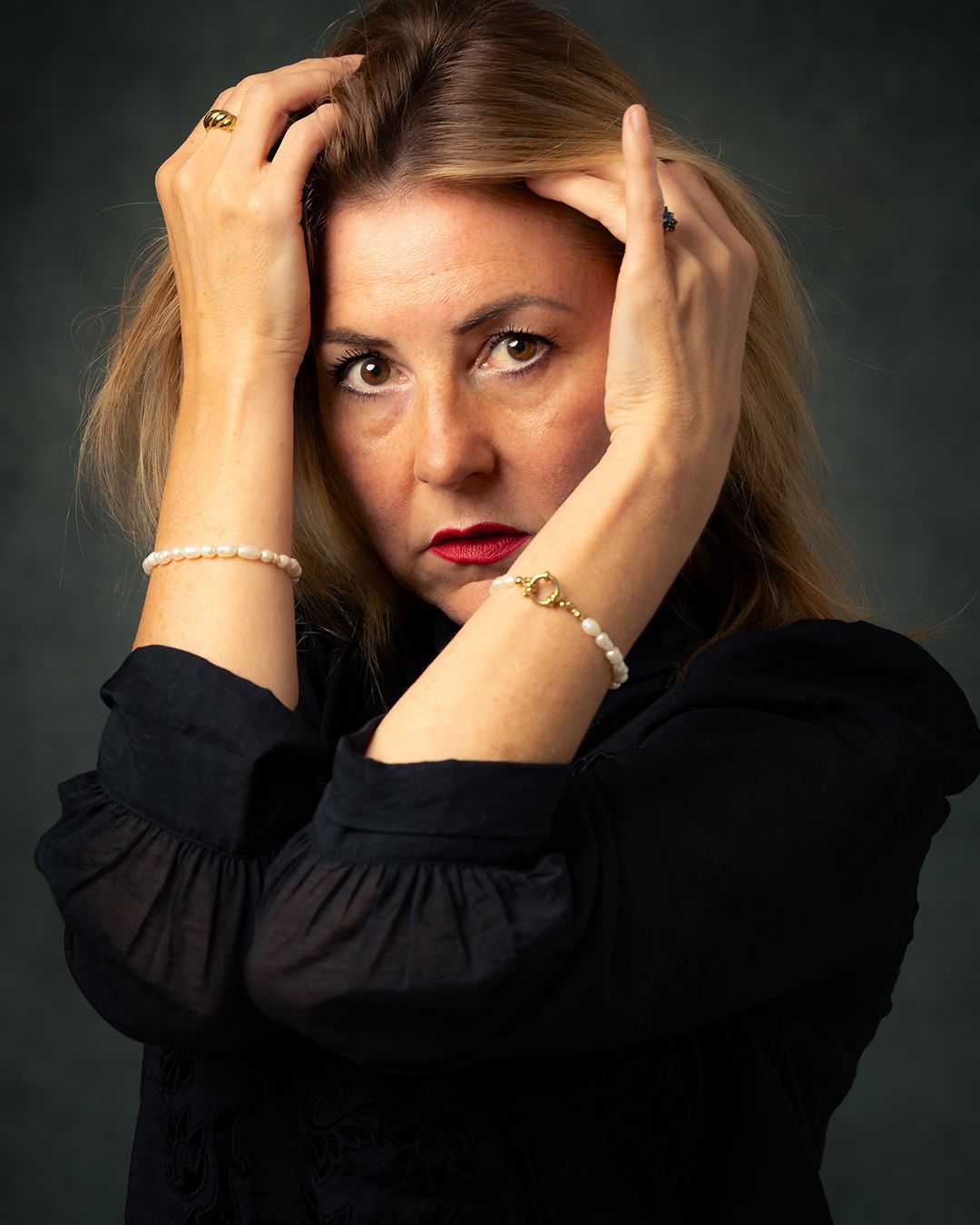 Vrouw met handen in het haar, ziet er bezorgd uit, draagt een zwart topje en parels.