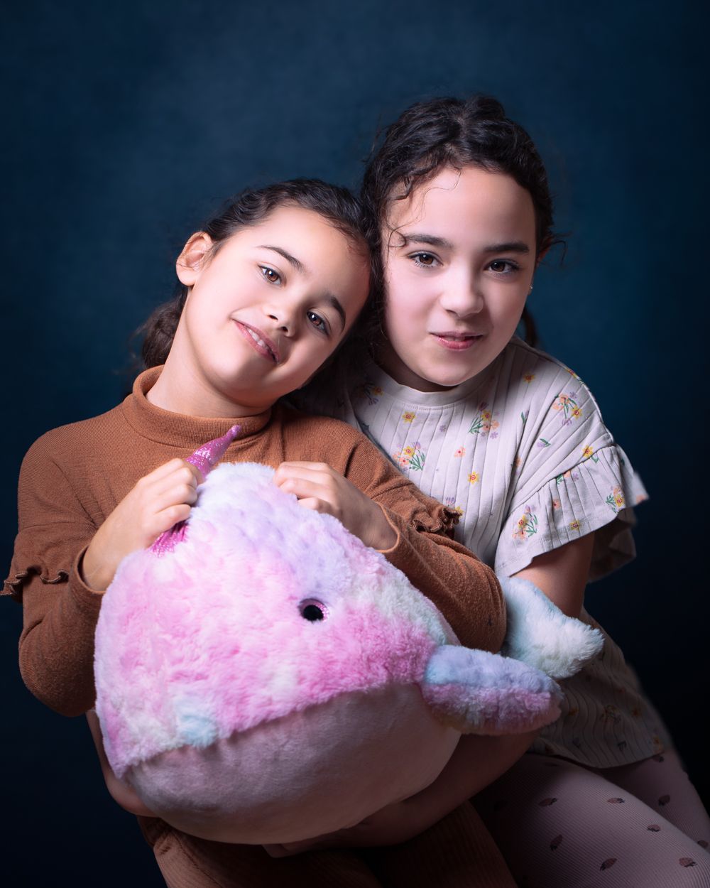 Twee meisjes knuffelen een roze en blauwe walvisknuffel. Donkerblauwe achtergrond.