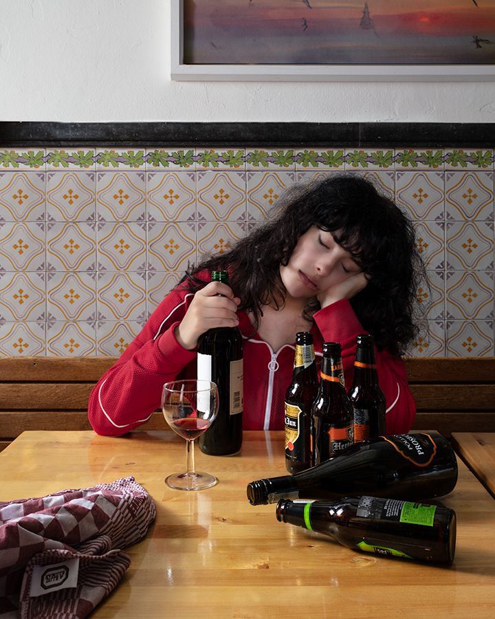 Een vrouw zit aan een tafel met flessen bier en wijn