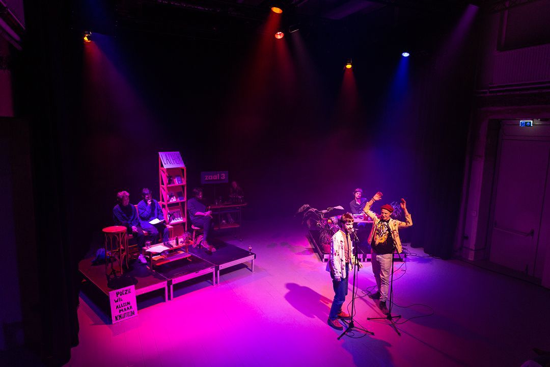 Een band treedt op op een podium verlicht met paarse en rode lampen. Muzikanten bespelen instrumenten.
