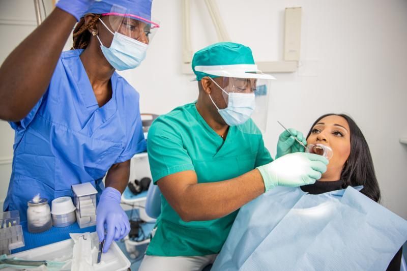 A woman is sitting in a dental chair getting her teeth examined by two dentists.