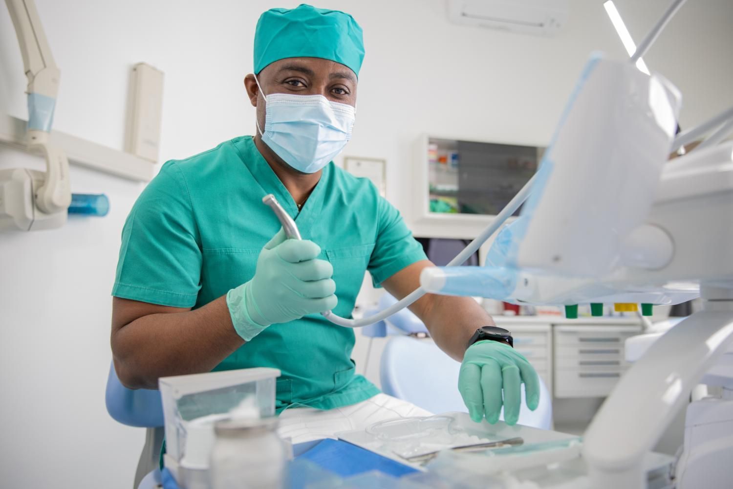 An oral surgeon wearing a mask and gloves is holding a toothbrush in a dental office.