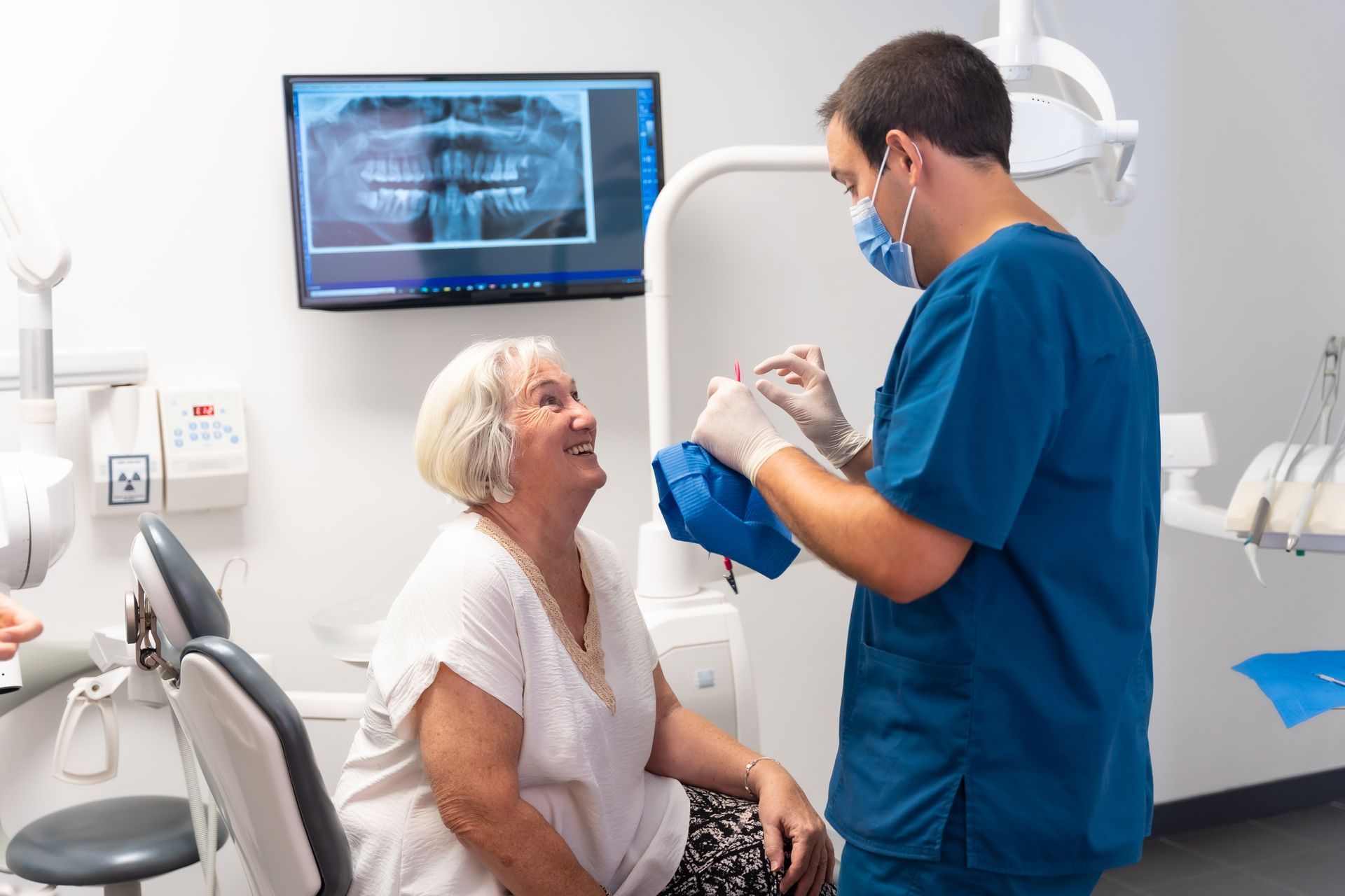 Dentist in blue scrubs showing x-ray to smiling patient in a dental exam room