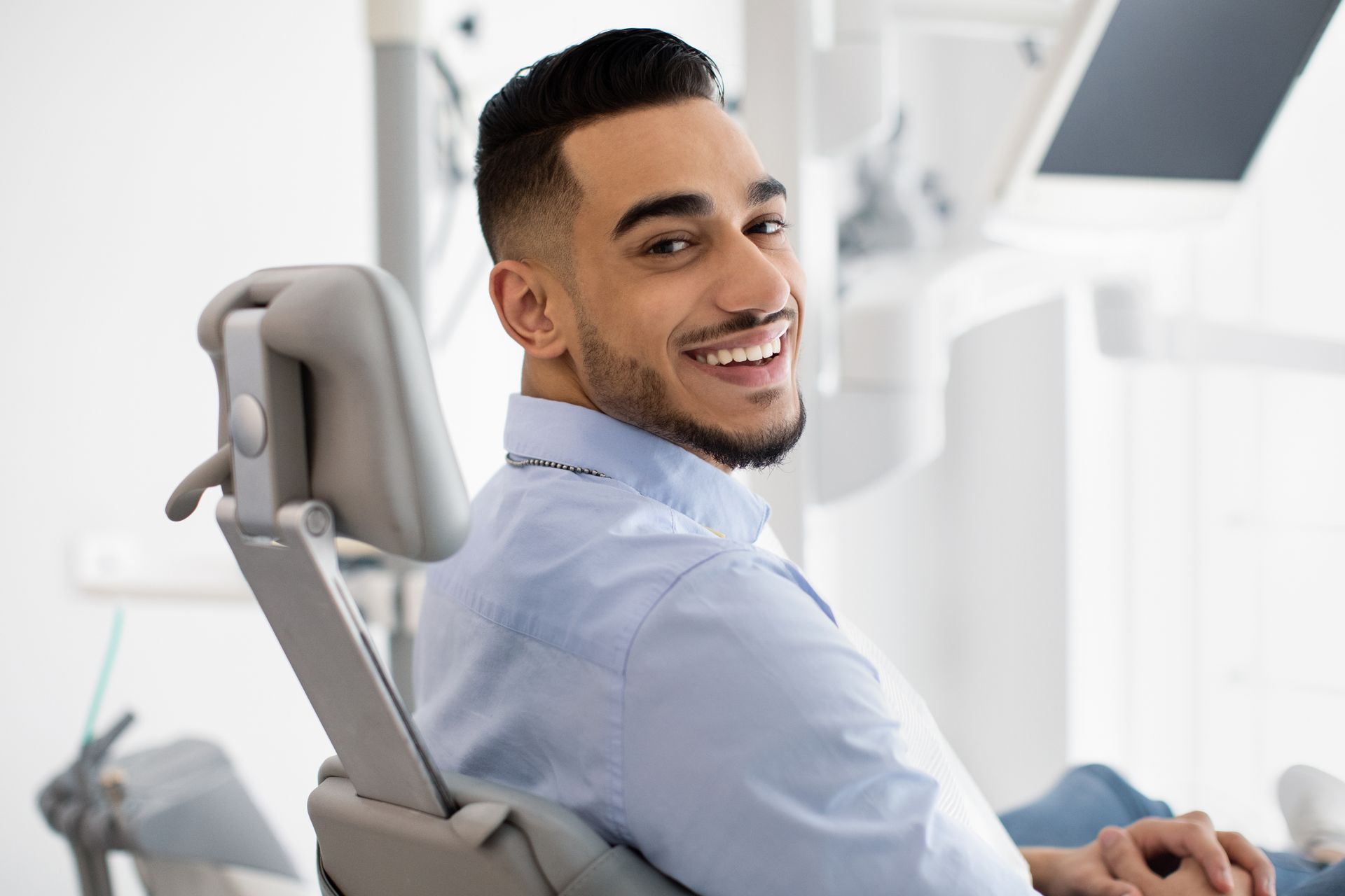 Man smiling in a dental chair. He is in a light blue shirt, looking at the camera.