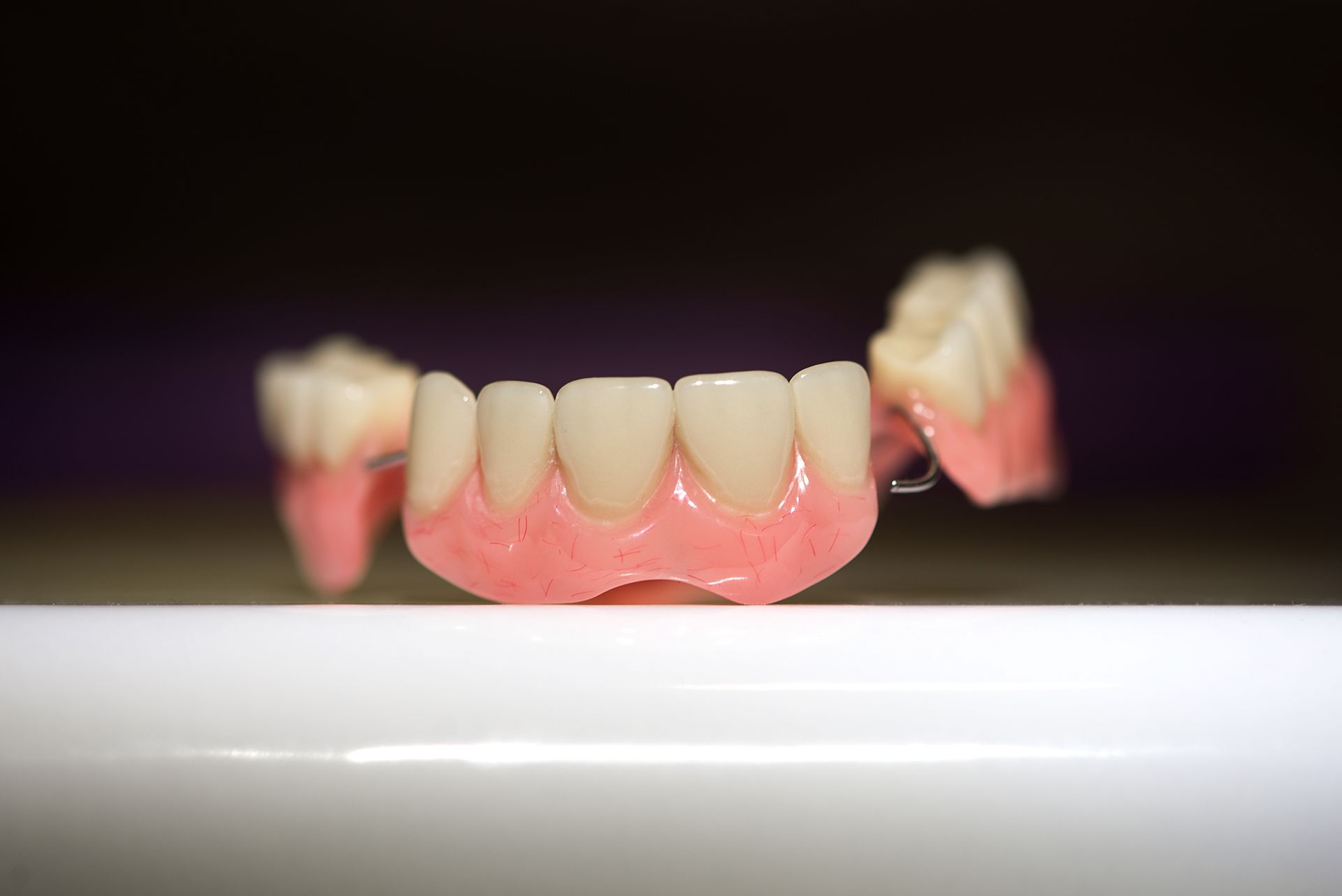 Partial dentures with pink base, white teeth, and metal clasps, resting on a white surface.