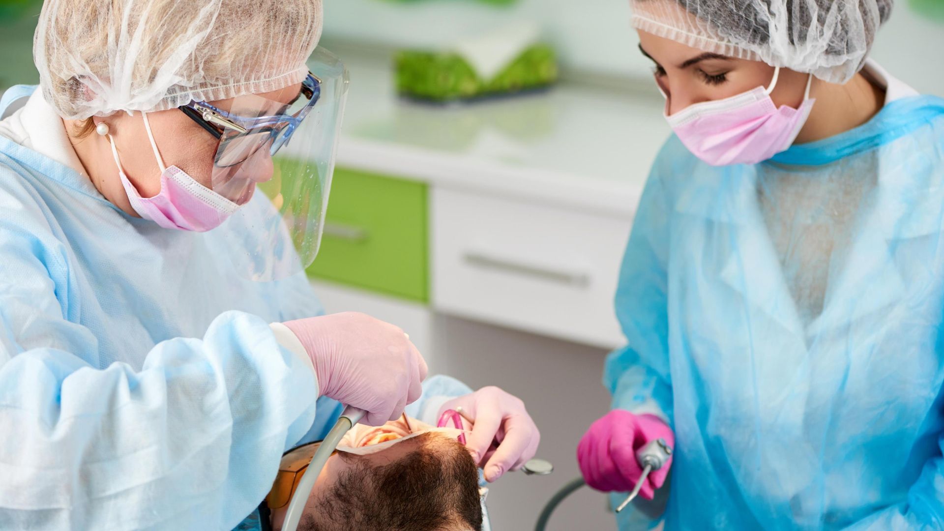 Two female dentists are working on a patient 's teeth in a dental office.