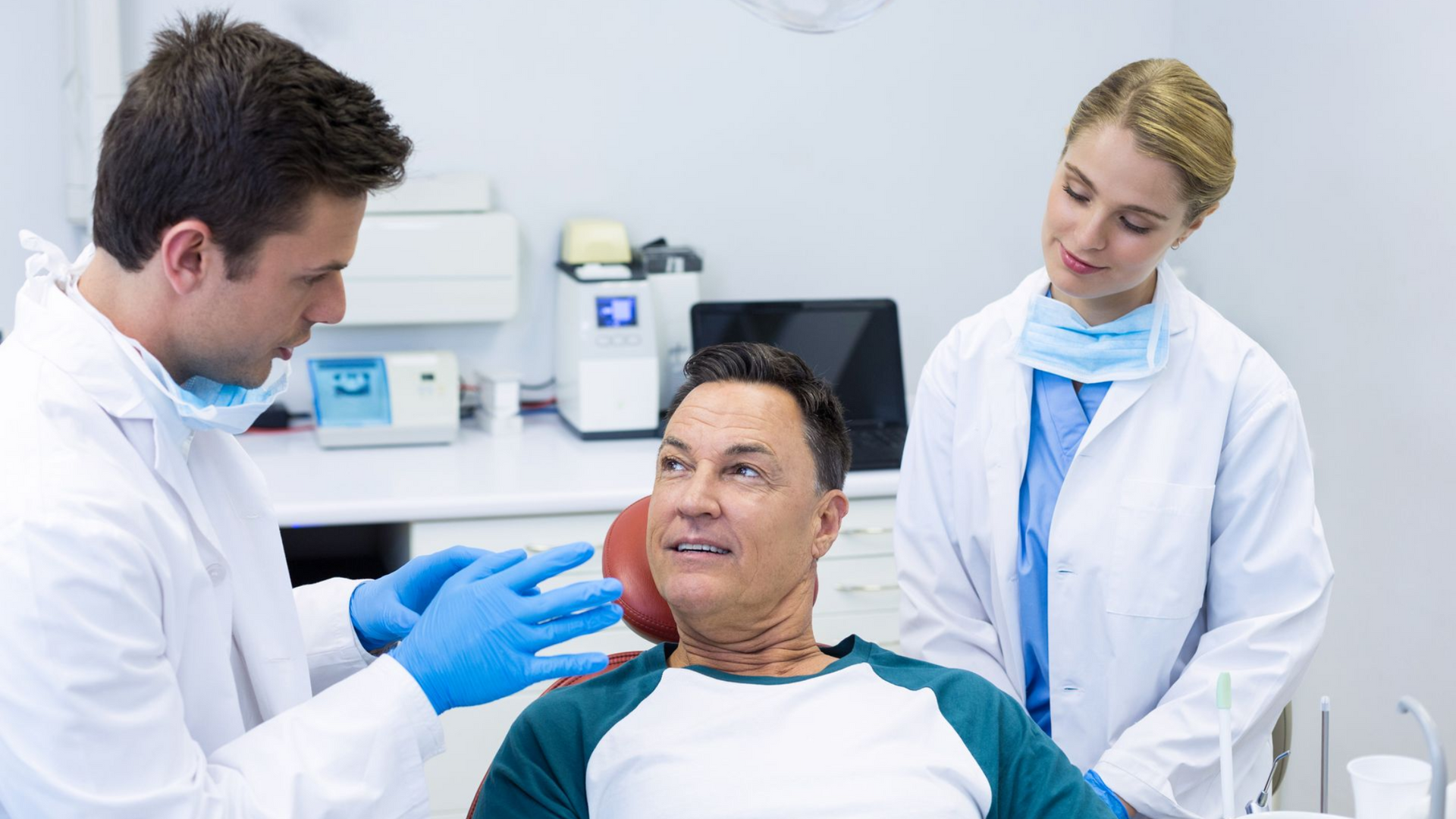 Dentist and assistant examining patient's mouth in a dental office.