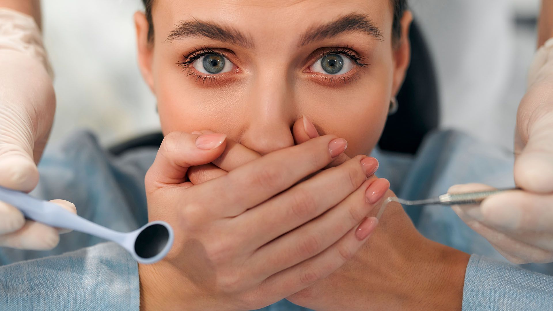 Woman with bad breath at the dentist, hand covering mouth