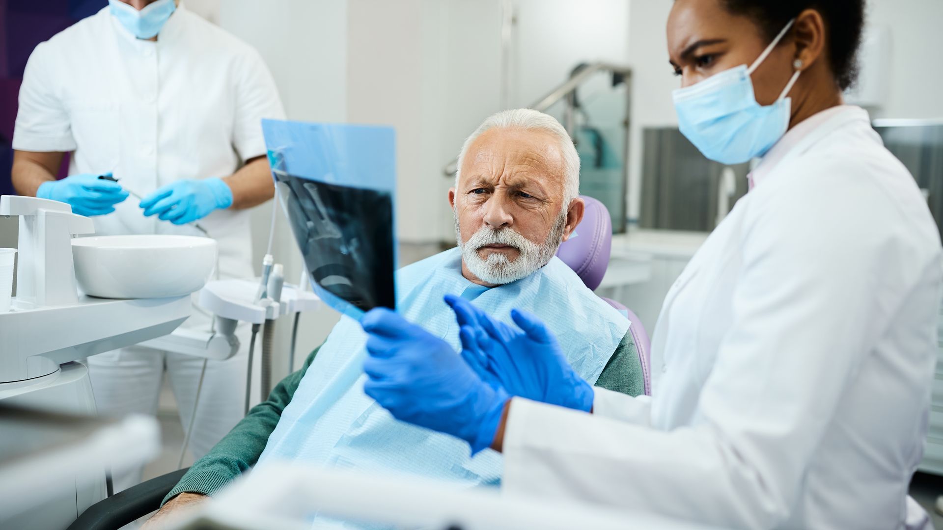 Dentist showing X-ray to a patient. Both wearing masks and gloves in a dental office.