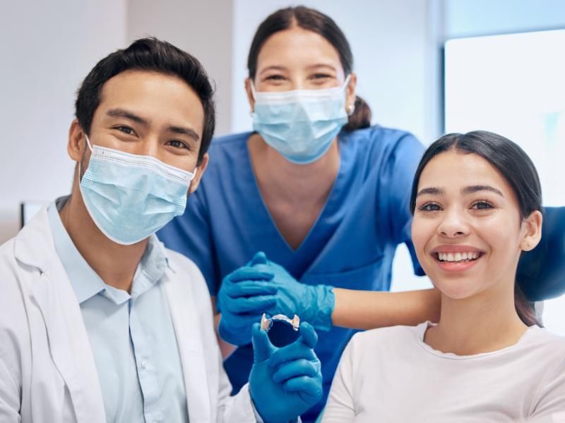 A dentist , nurse and patient are posing for a picture in a dental office.