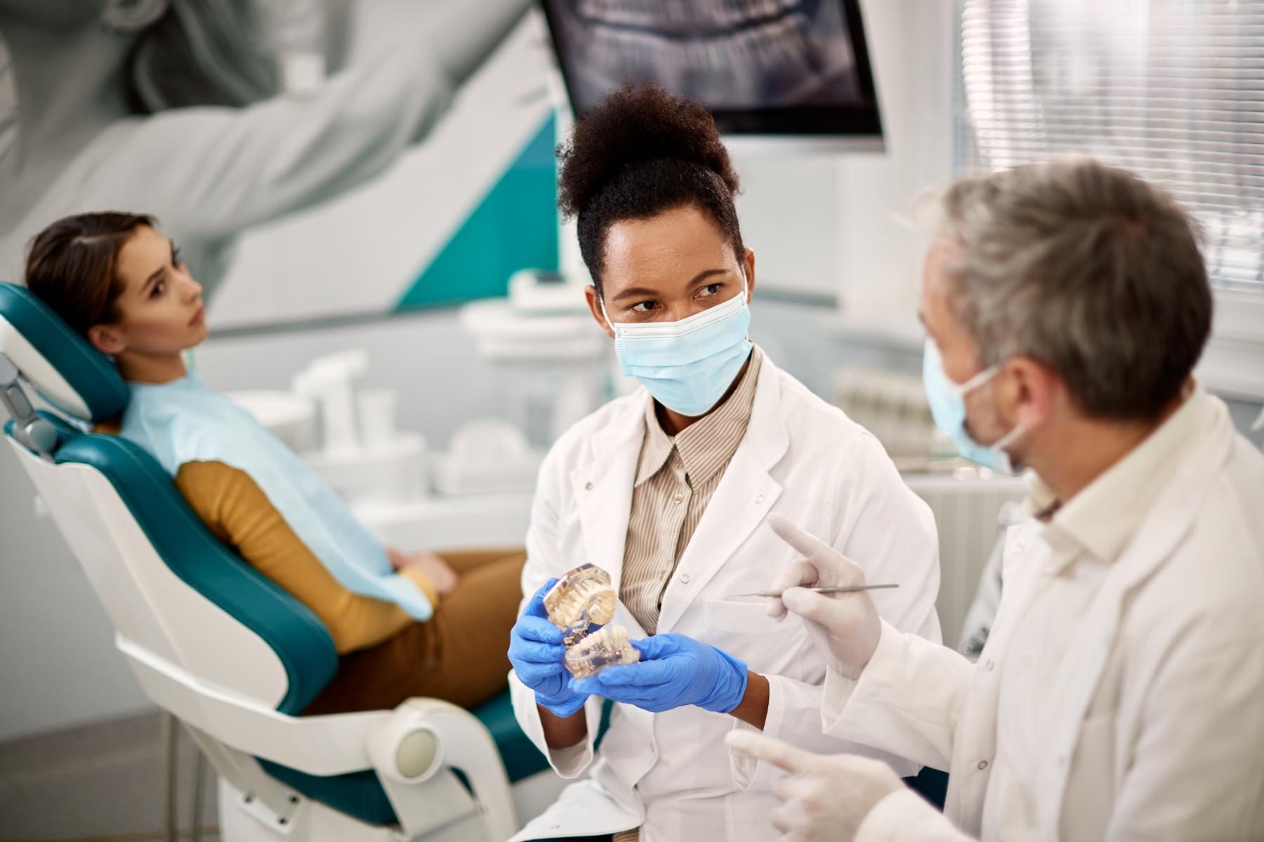 A woman is sitting in a dental chair talking to two dentists.