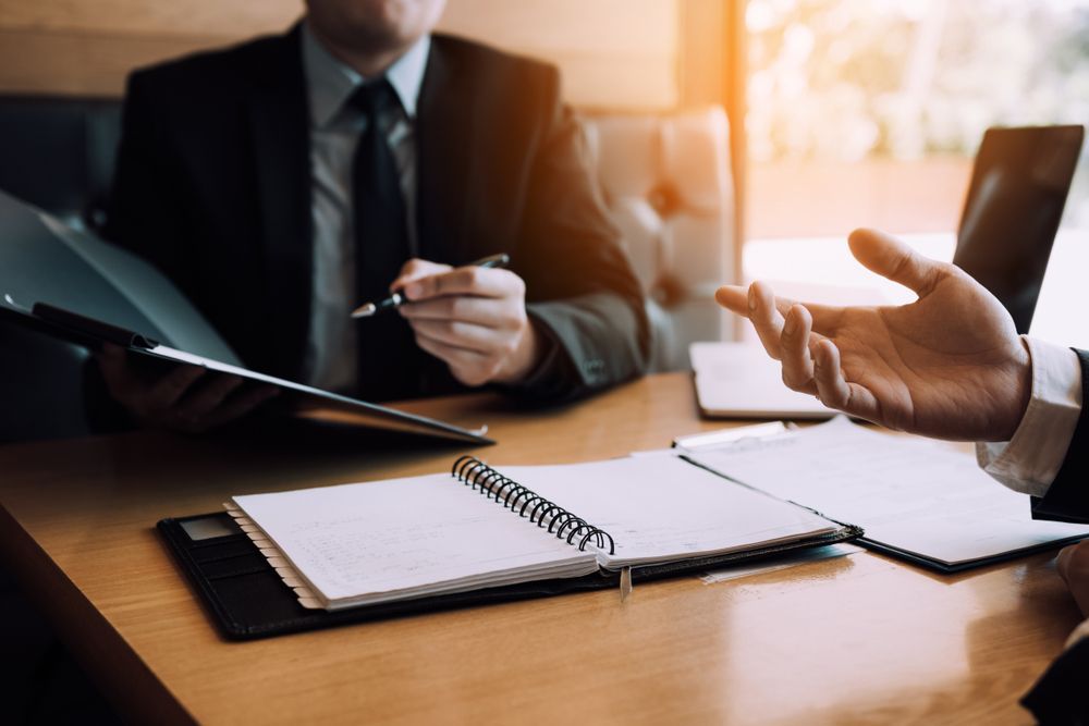 Two Suited People at a Table, One Gesturing — People Assured Partners in Cannonvale, QLD