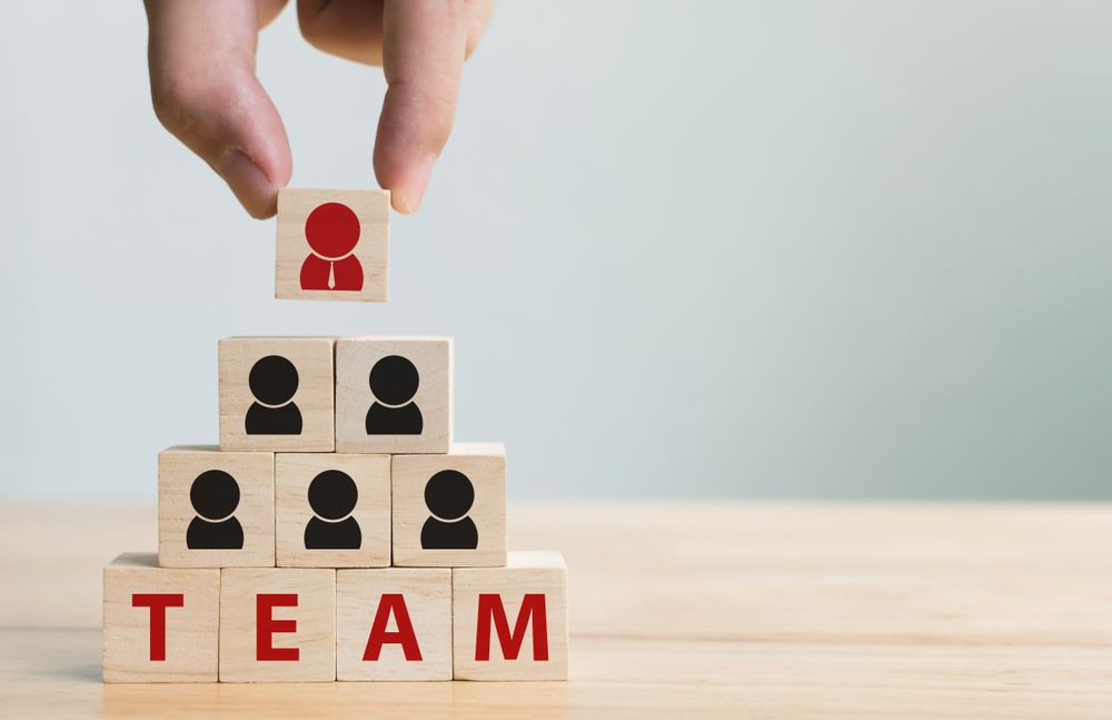 Hand Placing a Red Person Icon Block on Top of a Team Pyramid Made of Blocks — People Assured Partners in Cairns, QLD