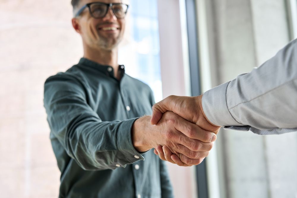 Man in Glasses Smiles, Shaking Hands With Another Person in an Office Setting — People Assured Partners in Bowen, QLD