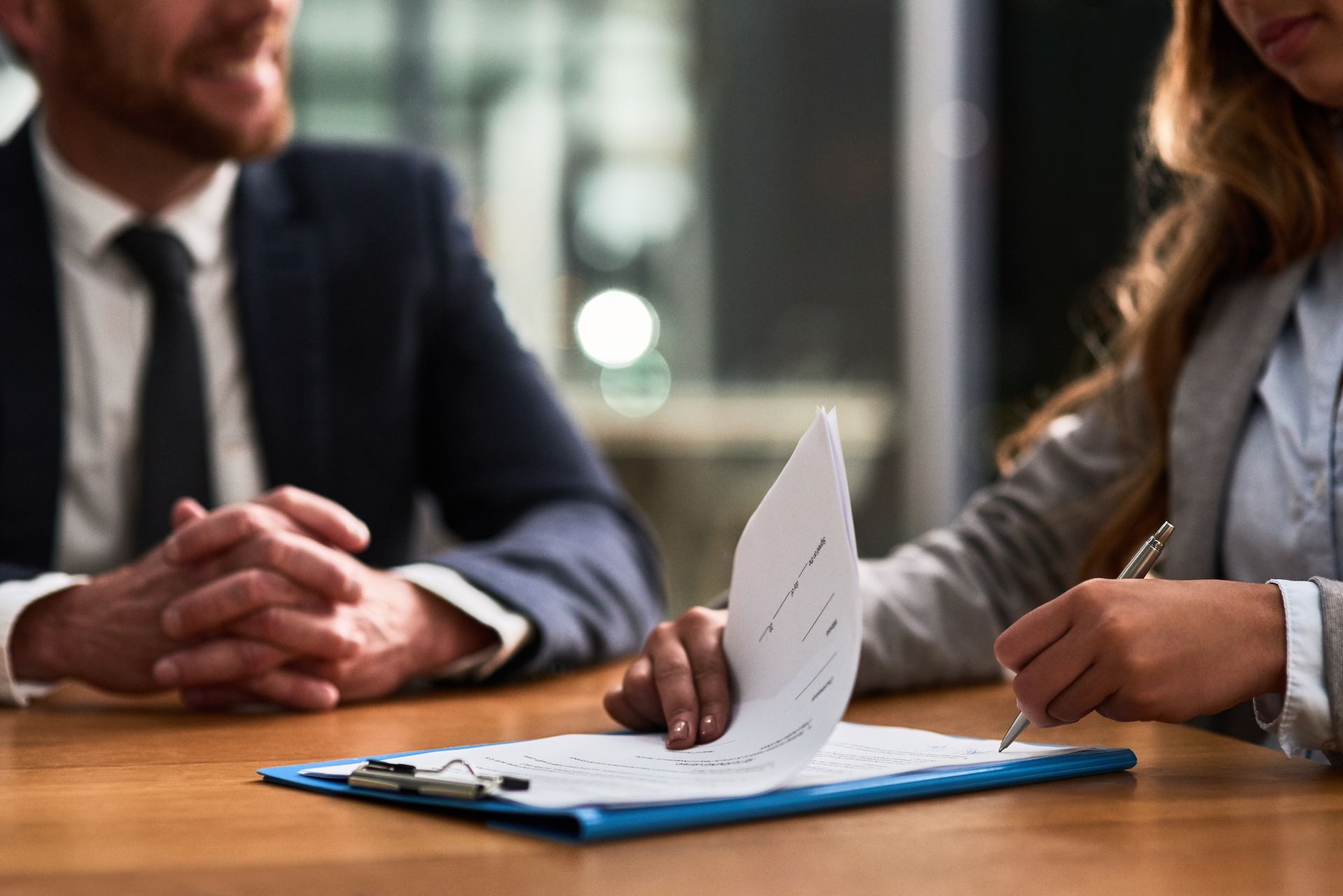 Man and Woman at Table, Woman Signing Document on Clipboard — People Assured Partners in Cannonvale, QLD