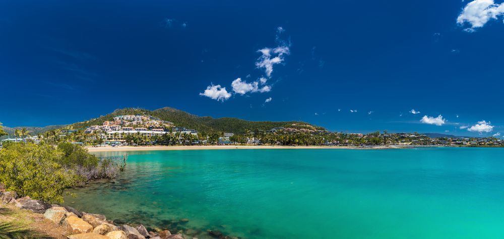 Turquoise Water With a Beach and Buildings Along the Shore — People Assured Partners in Airlie Beach, QLD