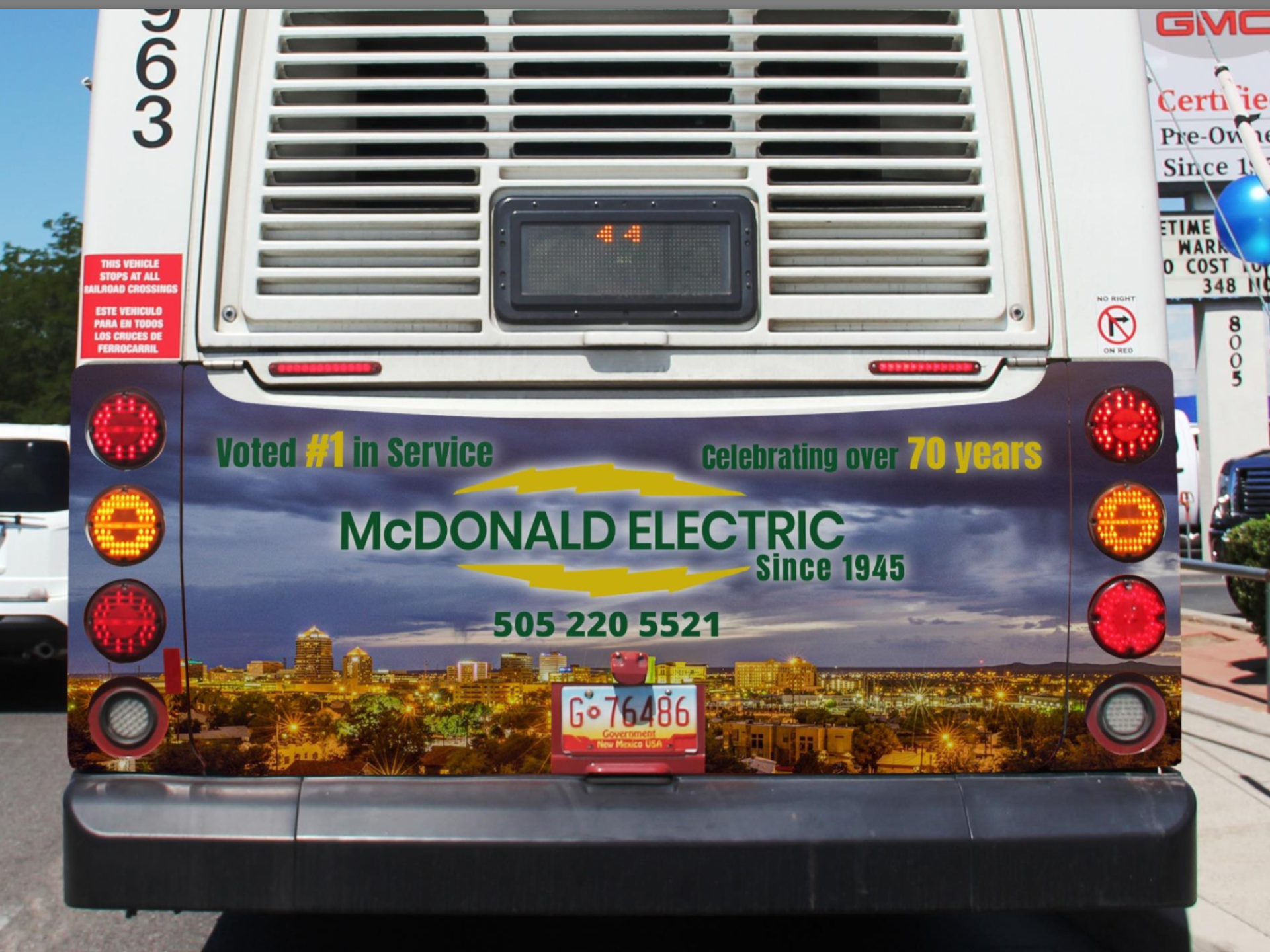 Rear of a bus with a McDonald Electric advertisement featuring a city skyline, phone number, and 