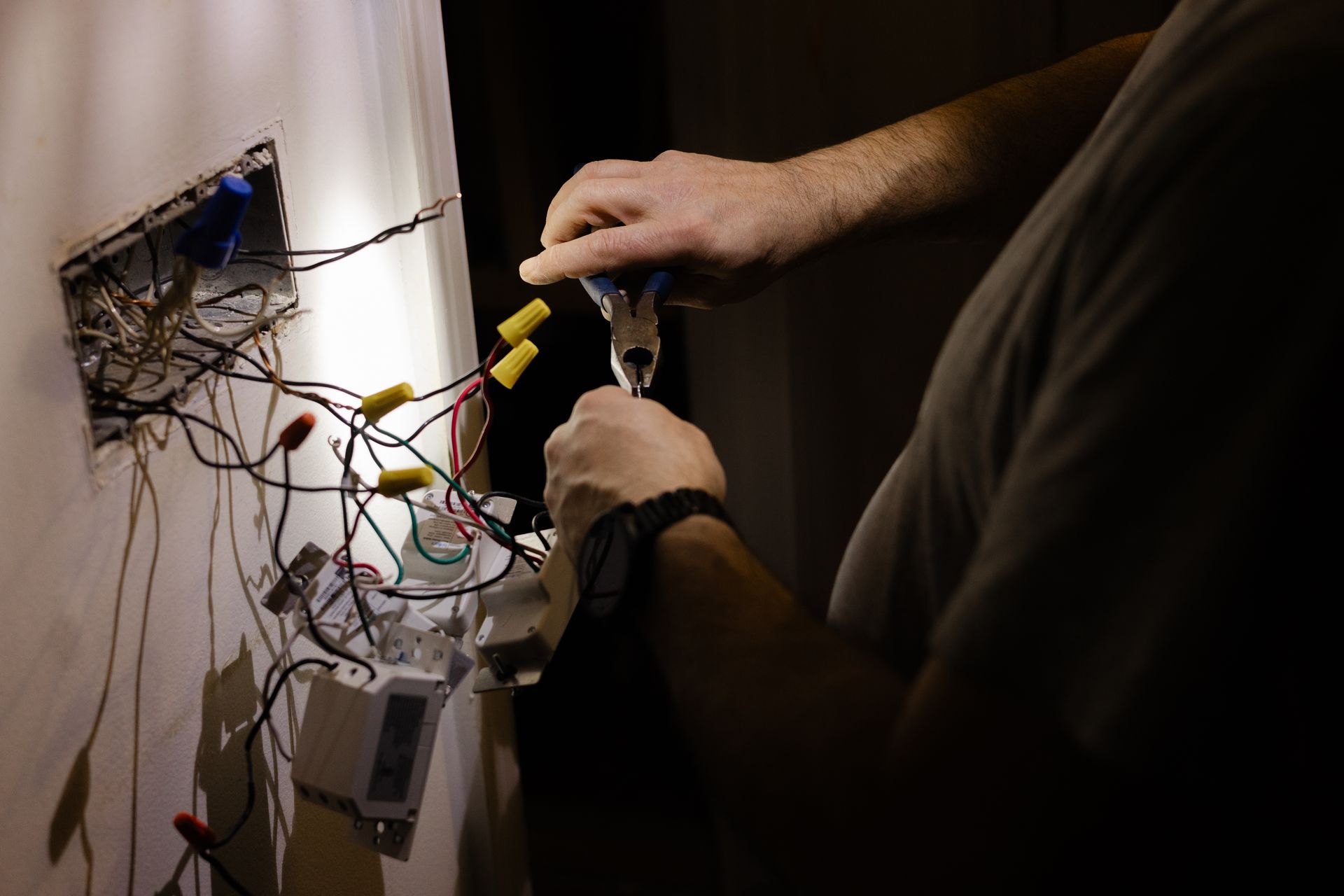 Electrician repairing exposed wiring and connections in a wall outlet.