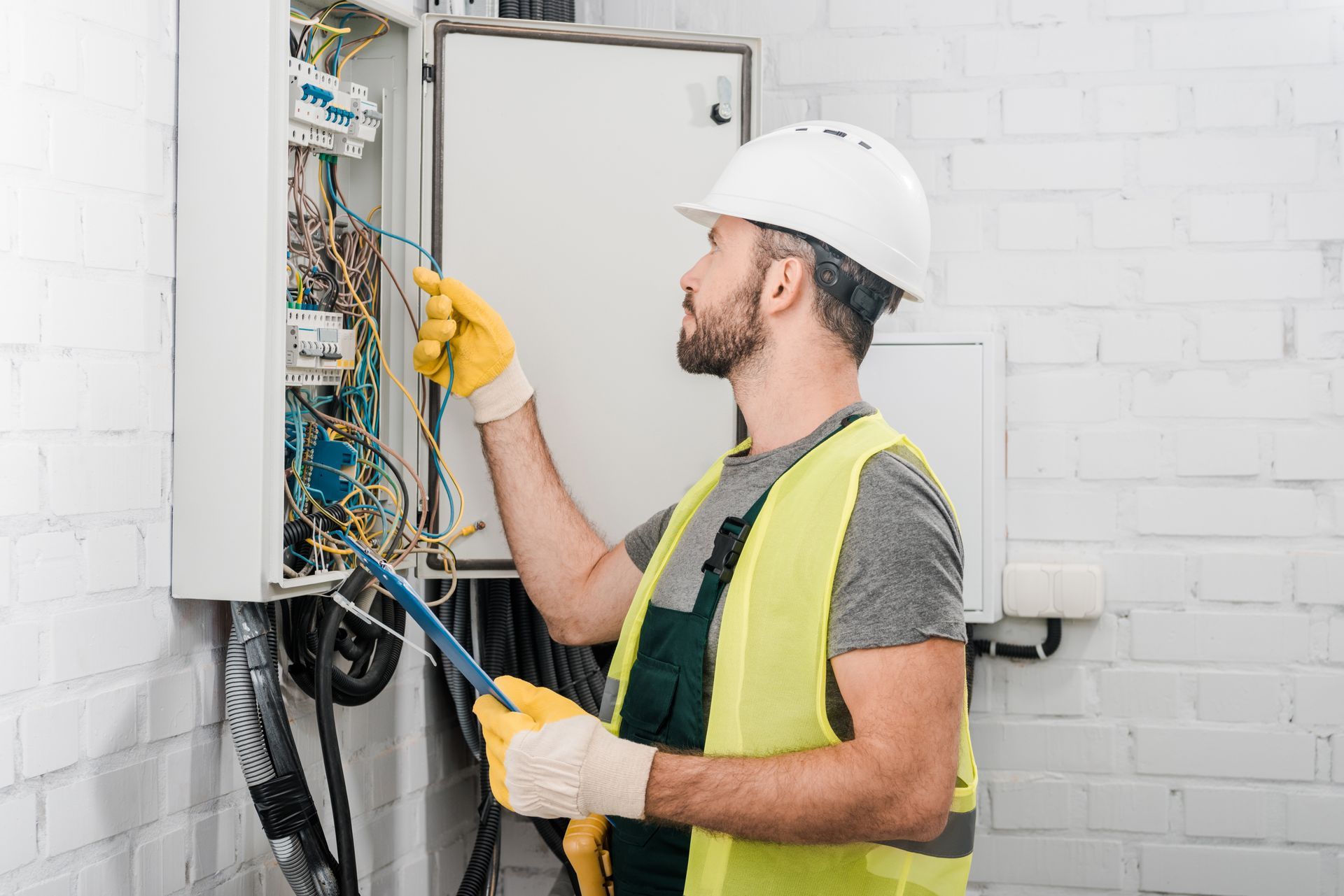 Electrician wearing safety gear inspecting and wiring an electrical panel.