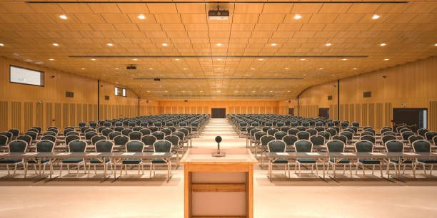 A large auditorium with rows of chairs and a podium with a microphone in the middle.