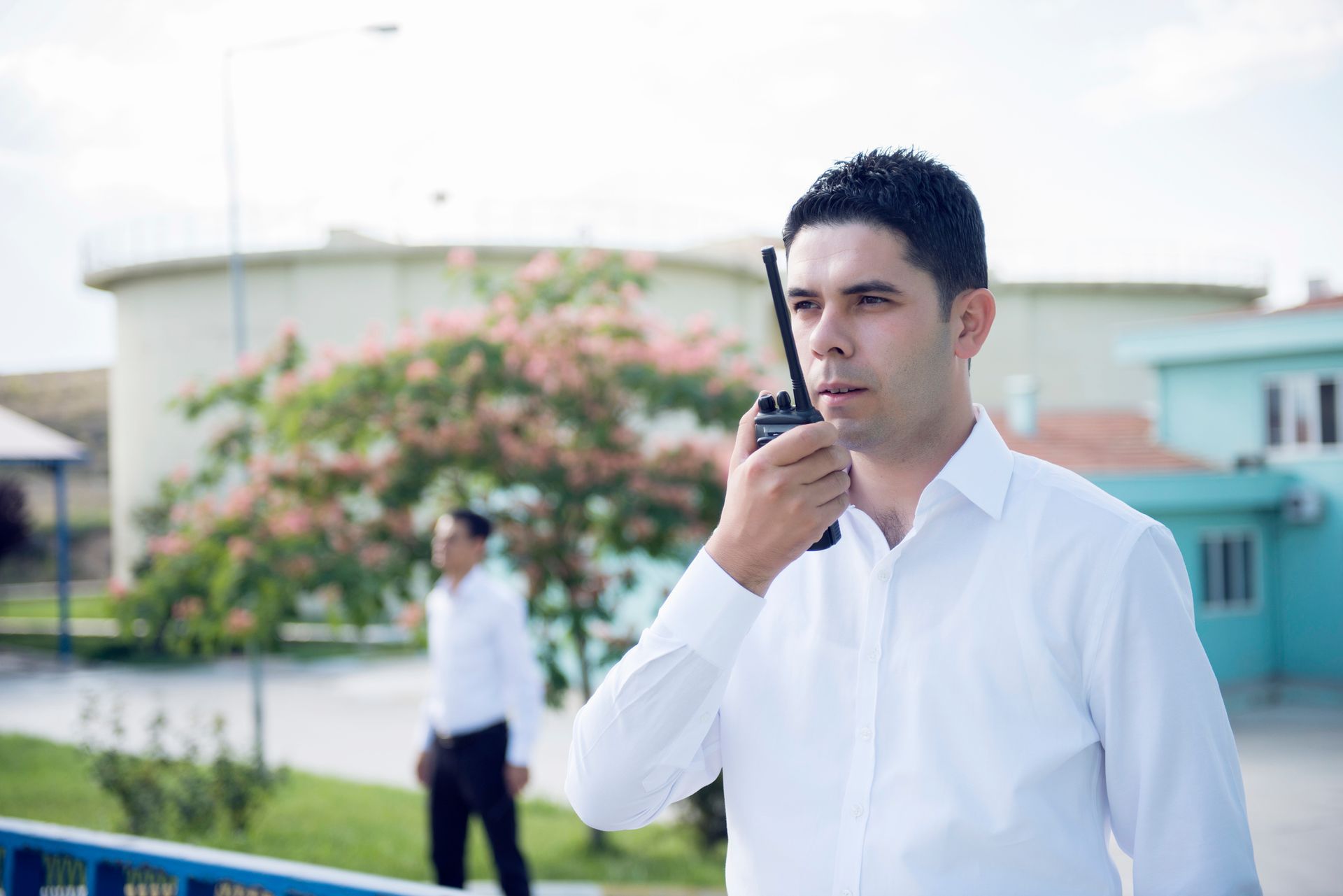 A man in a white shirt is talking on a walkie talkie.